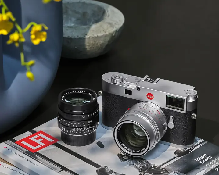 Leica camera and lens on top of two books, with a vase of flowers in the background.